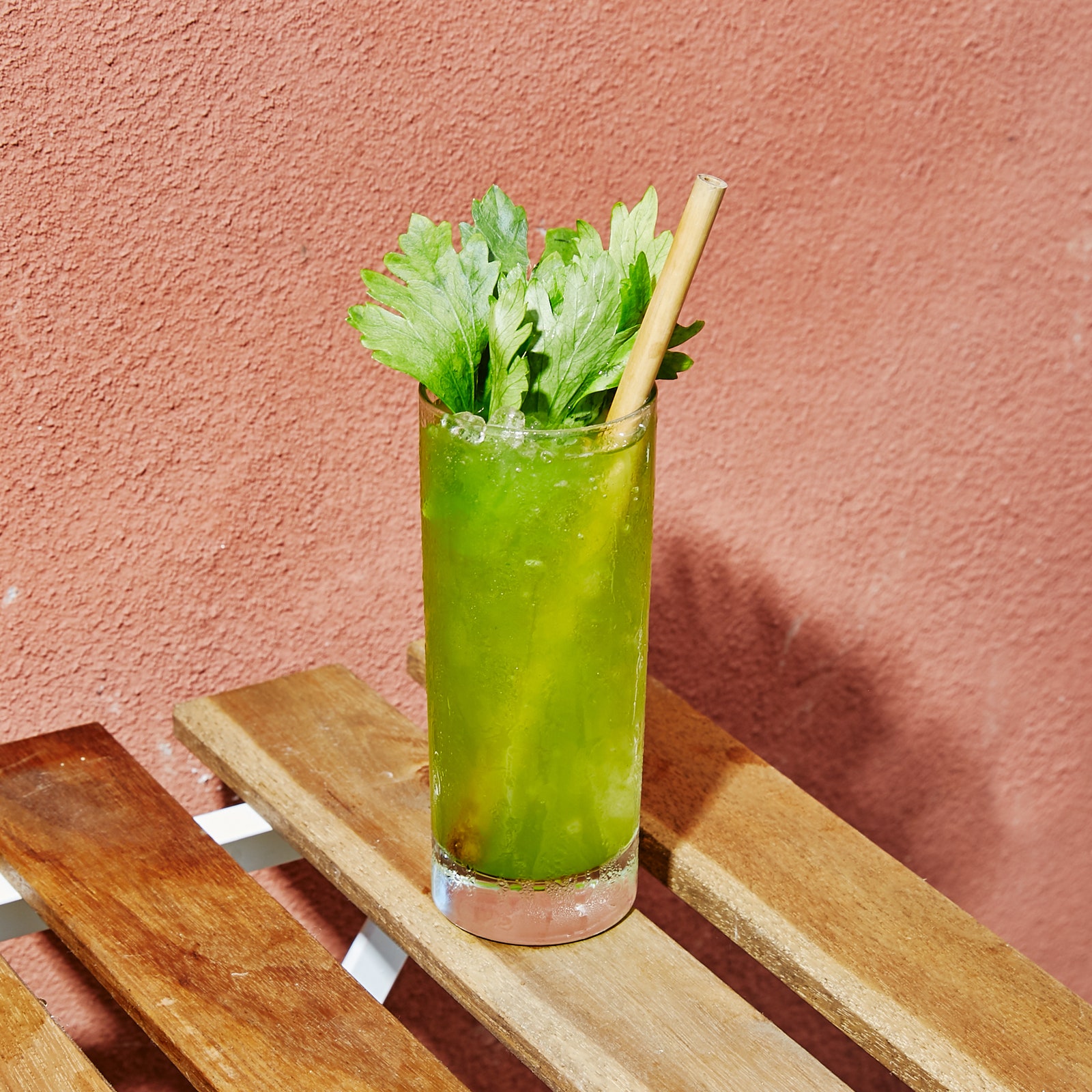 A green cocktail in a tall highball glass with a leafy garnish sits on a table outside Hunky Dory.