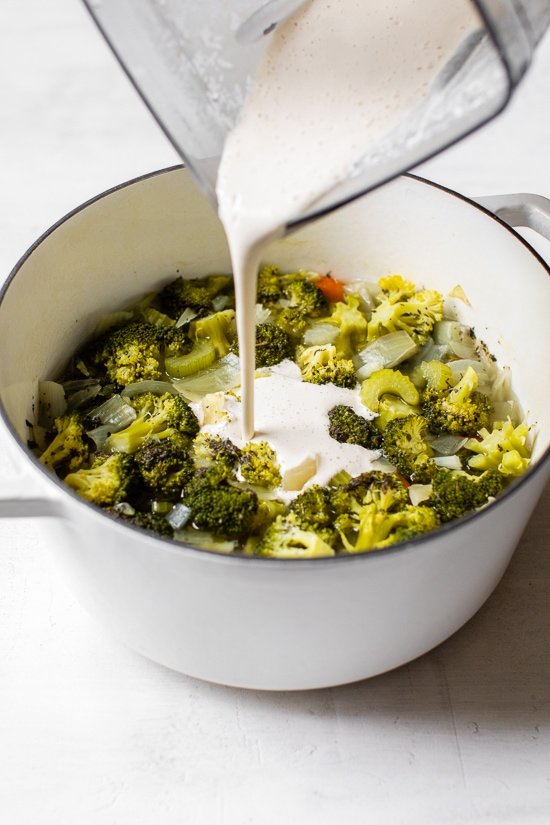 Pouring cashew milk into a pot of cooked vegetables.